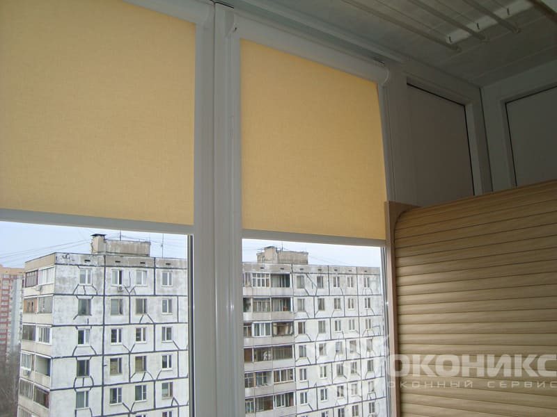 Остеклённый балкон с рулонными шторами пастельного оттенка — демонстрация практичности и стиля в оформлении оконных проёмов.